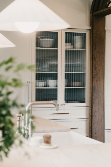 cuisine Ateliers Jacob avec armoires vitrées en verre cannelé, rangement sur mesure et détails en bois chaleureux intégrés à un îlot en pierre