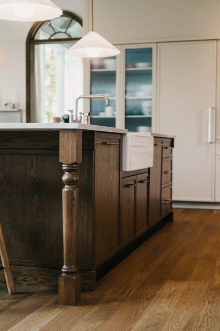 cuisine Ateliers Jacob avec îlot en bois massif sur mesure, comptoir en pierre clair, évier tablier intégré et détails de menuiserie travaillés pour un aménagement chaleureux et fonctionnel