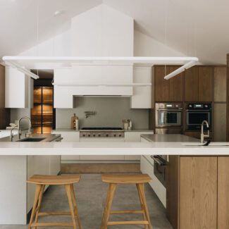 Cuisine contemporaine haut de gamme aux lignes épurées, combinant armoires en bois naturel et surfaces blanches, avec îlot central fonctionnel, hotte architecturale encastrée et électroménagers intégrés, créant un espace lumineux et équilibré pensé pour l’ergonomie et la fluidité des usages.