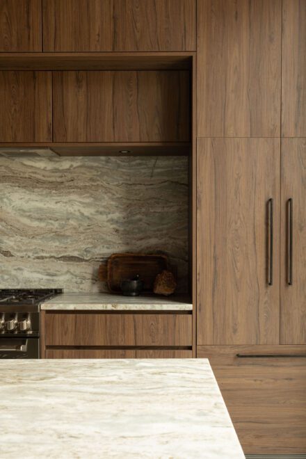 Cuisine Ateliers Jacob avec grand îlot en quartzite effet cascade, armoires en noyer foncé et dosseret en pierre naturelle dans une cuisine moderne haut de gamme.