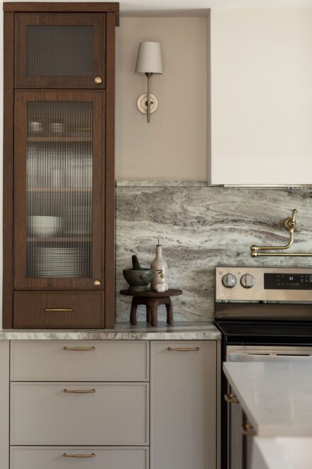 Cuisine Ateliers Jacob avec vitrine en bois foncé et verre cannelé, comptoir en quartzite et détails en laiton dans une cuisine raffinée.