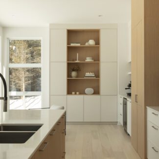 Cuisine lumineuse Ateliers Jacob avec îlot central en quartz, armoires en bois blanc et vue sur la forêt dans une résidence contemporaine