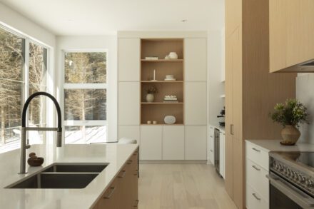 Cuisine lumineuse Ateliers Jacob avec îlot central en quartz, armoires en bois blanc et vue sur la forêt dans une résidence contemporaine