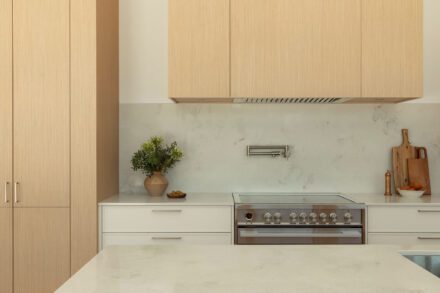 Cuisine Ateliers Jacob avec armoires en bois clair, comptoir en quartz blanc, hotte intégrée et dosseret minéral dans une résidence contemporaine à Piedmont