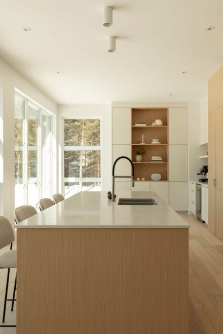 Cuisine lumineuse Ateliers Jacob avec îlot central en quartz, armoires en bois blanc et vue sur la forêt dans une résidence contemporaine à Piedmont