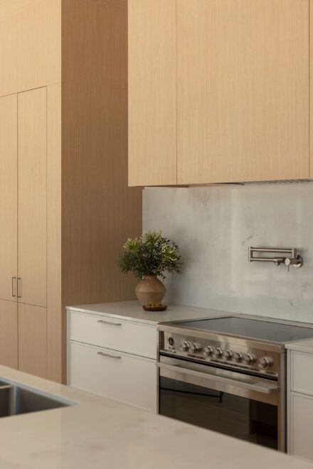 Cuisine Ateliers Jacob avec armoires en chêne clair, dosseret effet pierre et cuisinière en acier inoxydable dans une résidence contemporaine haut de gamme dans les Laurentides