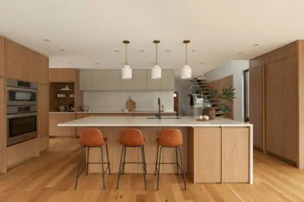 Cuisine Ateliers Jacob en chêne blanc et quartz avec grand îlot central, électroménagers encastrés, armoires minimalistes et aménagement contemporain lumineux à Montréal.