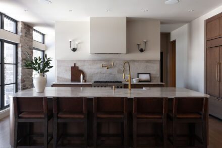 Cuisine Ateliers Jacob avec îlot arrondi en quartzite naturel et armoires en bois foncé dans une ambiance chaleureuse et contemporaine