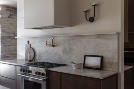 Cuisine Ateliers Jacob avec dosseret en quartzite naturel, armoires en bois brun foncé et robinetterie en laiton