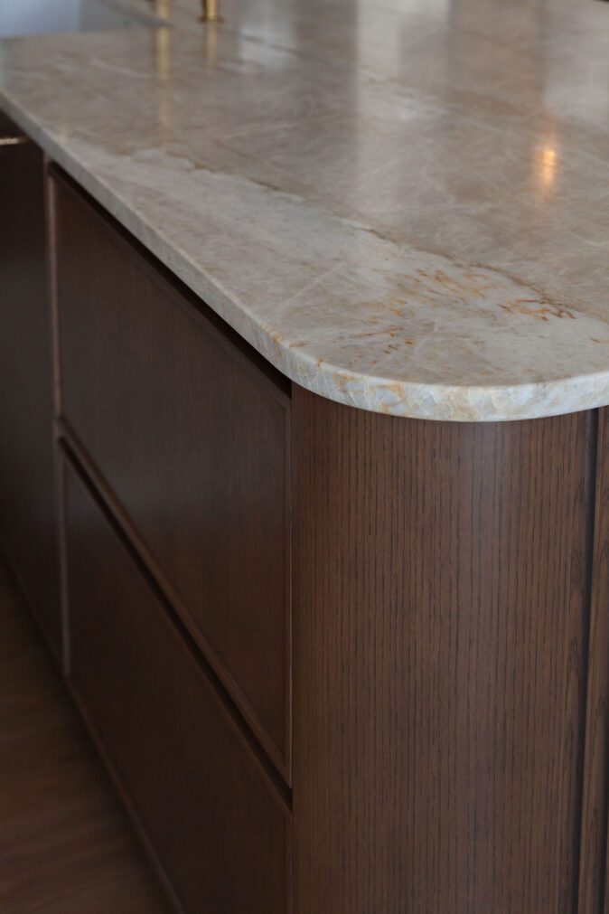 Détail de l’îlot Ateliers Jacob avec comptoir en quartzite naturel aux coins arrondis et armoires en bois foncé sur mesure dans une cuisine haut de gamme