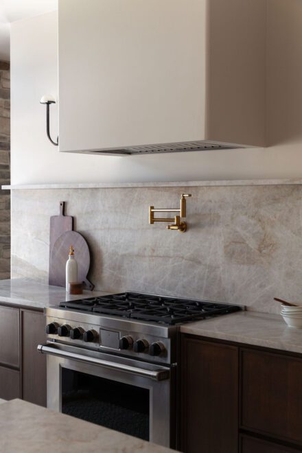 Cuisine Ateliers Jacob avec dosseret en quartzite naturel, armoires en bois foncé et robinetterie en laiton dans une cuisine haut de gamme intemporelle