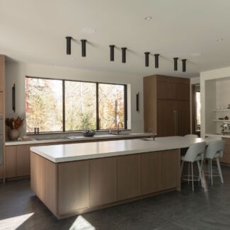 Grande cuisine haut de gamme Ateliers Jacob avec îlot central en porcelaine, armoires en chêne, électroménagers encastrés et vaste fenestration donnant sur la nature.