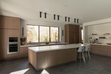 Grande cuisine haut de gamme Ateliers Jacob avec îlot central en porcelaine, armoires en chêne, électroménagers encastrés et vaste fenestration donnant sur la nature.