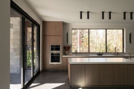 Cuisine minimaliste Ateliers Jacob avec îlot en porcelaine, mobilier en chêne sur mesure et grandes portes vitrées créant une continuité entre l’intérieur et l’extérieur.