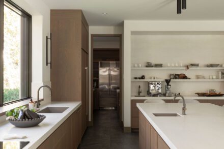 Cuisine contemporaine Ateliers Jacob avec deux éviers intégrés, armoires en chêne, îlot central en porcelaine et arrière-cuisine dissimulée dans un aménagement épuré.