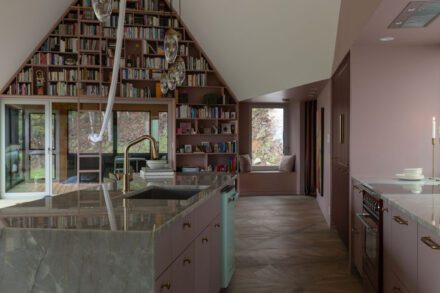 Cuisine Ateliers Jacob avec îlot en quartzite pleine hauteur, armoires rose bordeaux et bibliothèque sur mesure intégrée dans une aire ouverte lumineuse au design contemporain haut de gamme.