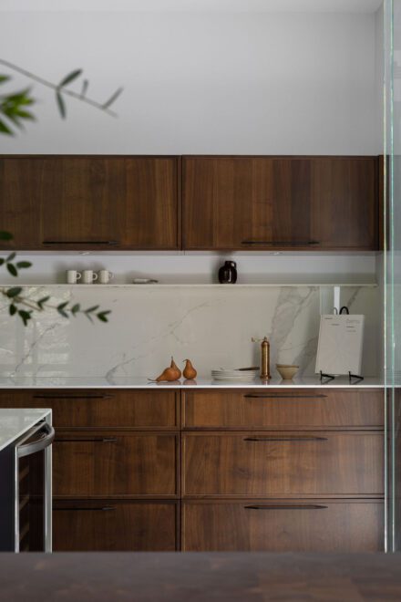 Cuisine haut de gamme Ateliers Jacob avec deux îlots en Dekton effet marbre, armoires en noyer foncé et grande fenestration ouverte sur la nature.