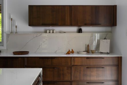 Cuisine Ateliers Jacob avec comptoir et dosseret en Dekton effet marbre, armoires en bois foncé et éclairage intégré dans une cuisine contemporaine minimaliste.