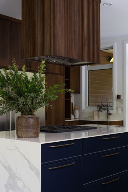 Cuisine haut de gamme Ateliers Jacob avec deux îlots en Dekton effet marbre, armoires en noyer foncé et grande fenestration ouverte sur la nature.