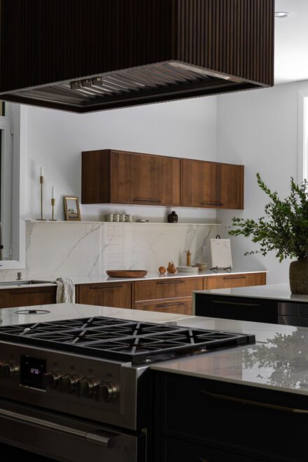 Cuisine haut de gamme Ateliers Jacob avec deux îlots en Dekton effet marbre, armoires en noyer foncé et grande fenestration ouverte sur la nature.