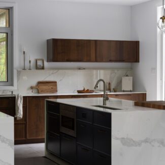 Cuisine haut de gamme Ateliers Jacob avec deux îlots en Dekton effet marbre, armoires en noyer foncé et grande fenestration ouverte sur la nature.