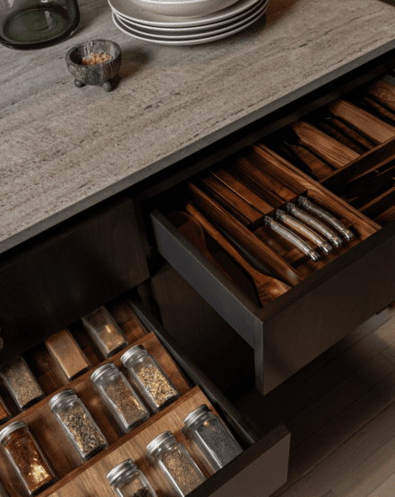 Custom storage by Ateliers Jacob: hardwood drawer dividers organize utensils and spices beneath a veined stone counter. Functional design, down to the detail.