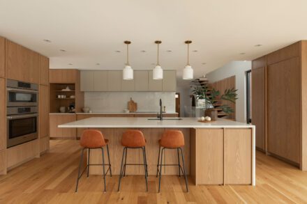 Cuisine contemporaine conçue par Ateliers Jacob avec armoires en chêne naturel, grand îlot central, comptoir de quartz blanc, dosseret effet marbre et trois tabourets en cuir cognac.