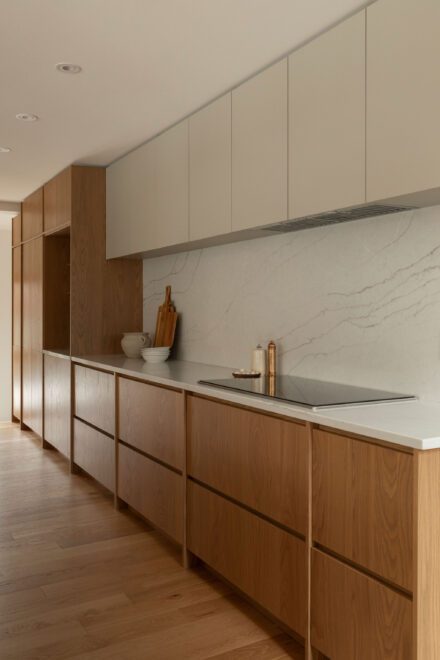 Cuisine Ateliers Jacob en chêne avec plaque à induction intégrée, comptoir de quartz blanc, dosseret effet marbre et armoires pleine hauteur.