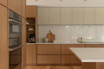 Cuisine Ateliers Jacob en chêne avec armoires pleine hauteur, dosseret en quartz effet marbre, comptoir de quartz blanc et fours encastrés Bosch.