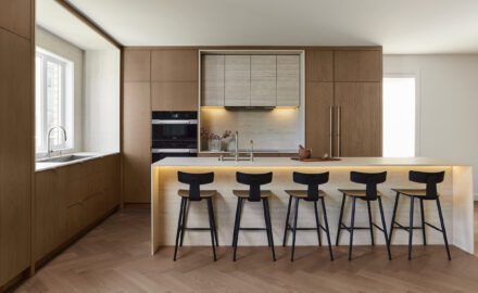 Cuisine moderne minimaliste en chêne signée Ateliers Jacob avec îlot en Dekton, plaque à induction intégrée, fours encastrés et réfrigérateur dissimulé derrière des panneaux de chêne.