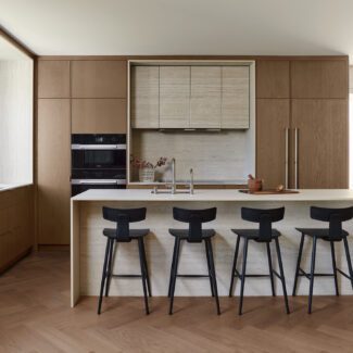 Cuisine moderne minimaliste en chêne signée Ateliers Jacob avec îlot en Dekton, plaque à induction intégrée, fours encastrés et réfrigérateur dissimulé derrière des panneaux de chêne.