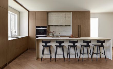 Cuisine moderne minimaliste en chêne signée Ateliers Jacob avec îlot en Dekton, plaque à induction intégrée, fours encastrés et réfrigérateur dissimulé derrière des panneaux de chêne.