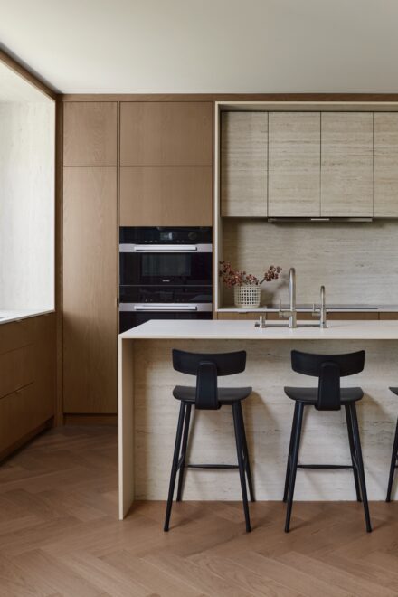 Cuisine moderne minimaliste en chêne réalisée par Ateliers Jacob avec îlot et comptoir en Dekton, plaque à induction intégrée, fours encastrés et rangement dissimulé.