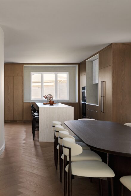 Cuisine moderne minimaliste en chêne signée Ateliers Jacob avec îlot en Dekton, plaque à induction intégrée, fours encastrés et réfrigérateur dissimulé derrière des panneaux de chêne.