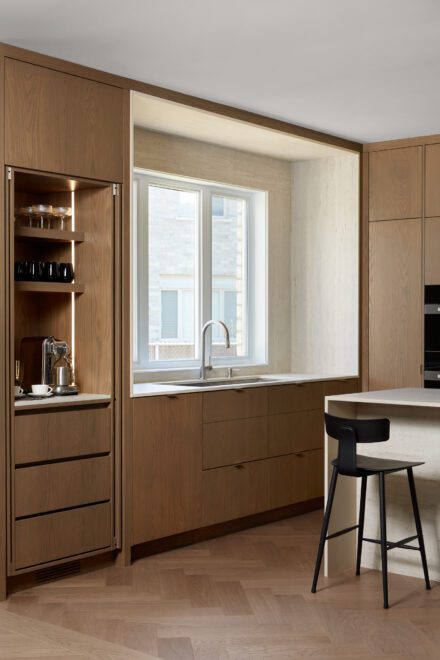 Cuisine moderne minimaliste en chêne réalisée par Ateliers Jacob avec comptoir en Dekton, évier sous fenêtre et coin café dissimulé derrière des portes escamotables.